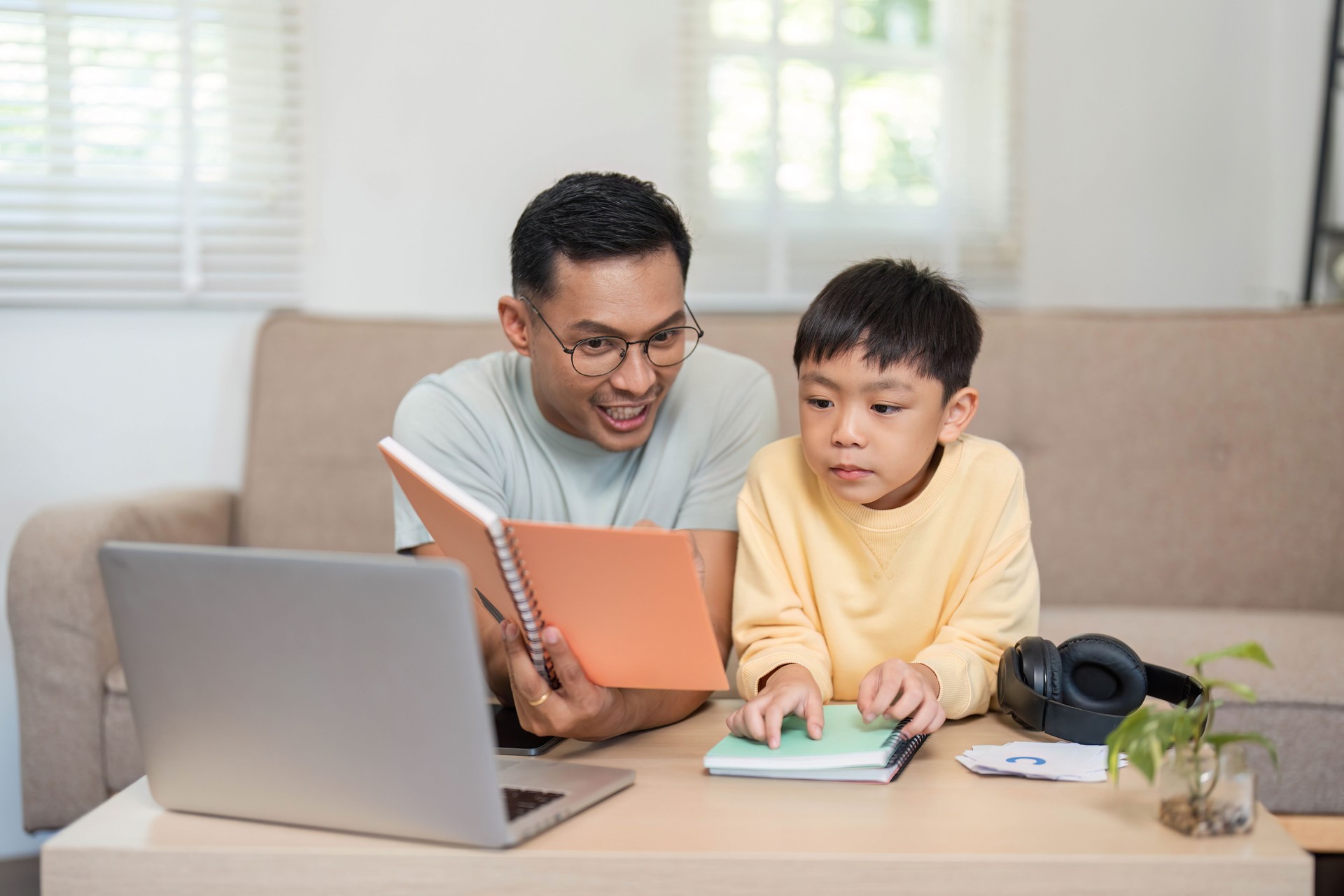 Homeschool father teaching son with notebook and laptop support
